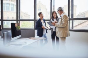 Trois collaborateurs, debout, échangent autour d'un dossier.