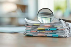 L'image montre une pile de dossier surmonté d'une loupe, symbolisant la perspective de voir de plus près quelle stratégie de test serait la plus adaptée.